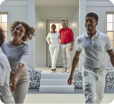 A man and woman standing at the front door with arms around each other, with two people in the forefront